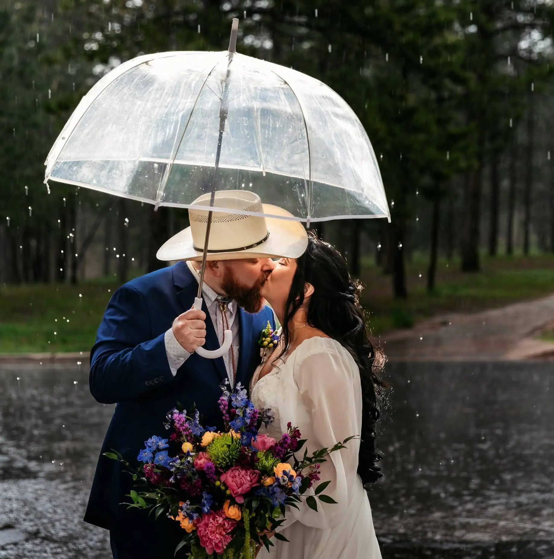 Rain at a wedding groom and bride kissing under umbrella at The Lodge at Cathedral Pines